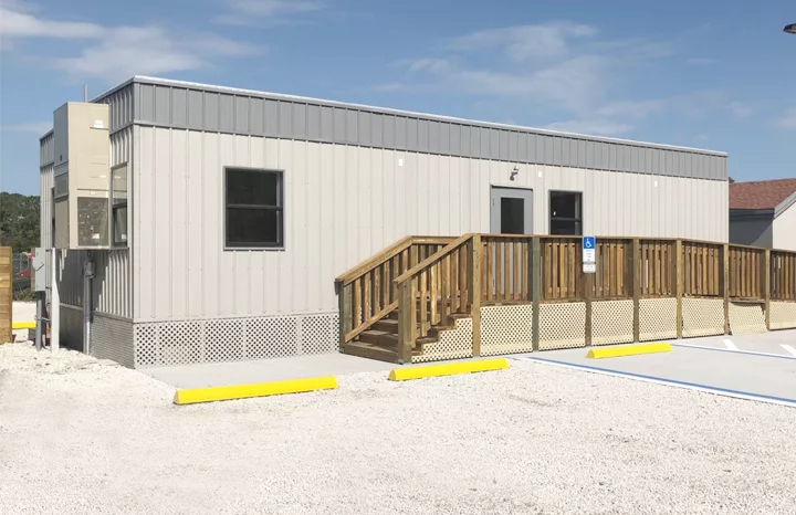 A business modular building attached to a wooden porch deck and a lattice fence skirt