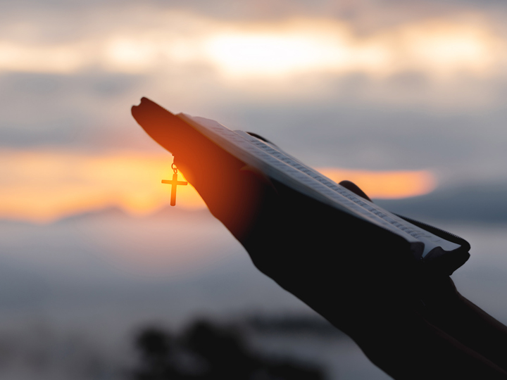 Person holding a bible at sunset