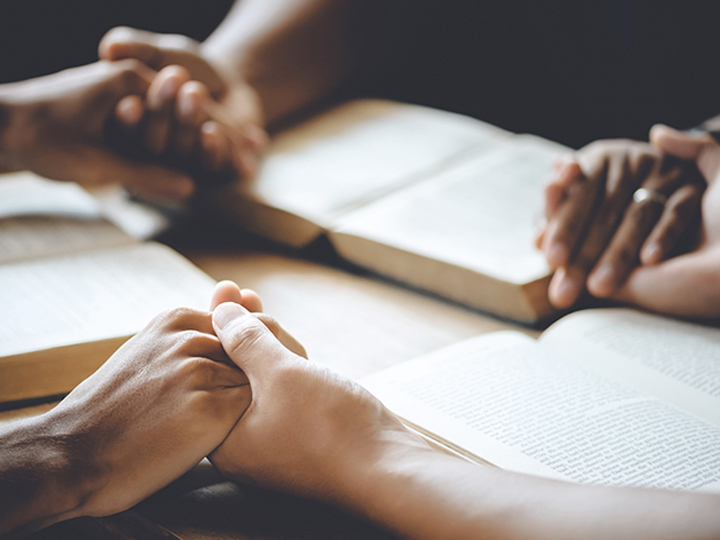 People holding hands with bibles praying